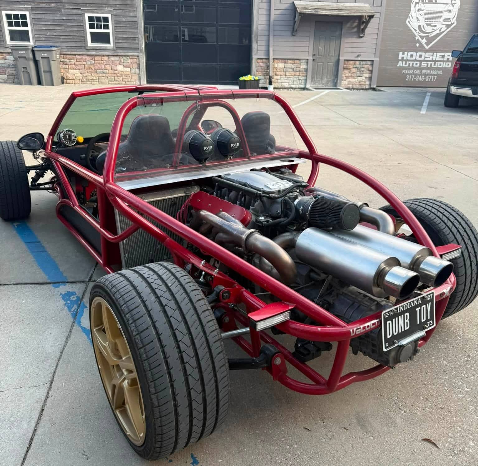 Custom red tube-frame car with exposed rear engine, exhaust system, and wide tires.